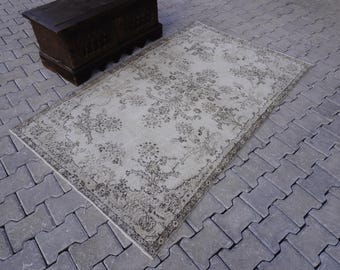 May include: A vintage-style rug with a floral pattern in shades of gray and white. The rug has a distressed look and is laid out on a gray concrete floor.