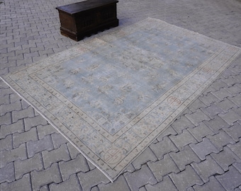 May include: A light blue rug with a beige border and a floral pattern. The rug is laid out on a gray brick patio.