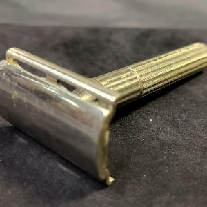 May include: A silver safety razor with a textured handle. The razor has a single blade and a chrome finish.