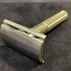 May include: A silver safety razor with a textured handle. The razor has a chrome finish and a safety bar.