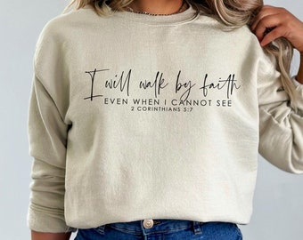 Puede incluir: Una sudadera de color beige claro con el texto "I will walk by faith EVEN WHEN I CANNOT SEE 2 CORINTHIANS 5:7" impreso en negro.