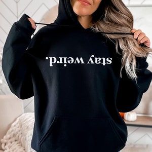 May include: Black hooded sweatshirt with the text "Stay Weird." printed in white on the front.