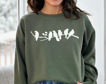May include: A green sweatshirt with a white silhouette of birds on a branch. The sweatshirt has a crew neck and long sleeves.