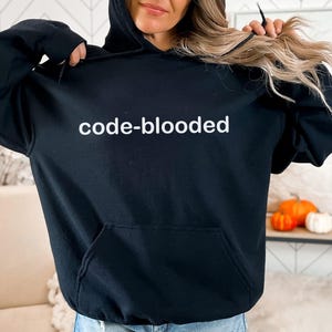 Op de afbeelding: Zwart hoodie met de tekst "code-blooded" in witte letters.