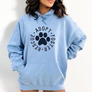 May include: A light blue hoodie with a navy blue paw print and the text "Adopt. Foster. Rescue." in a circle around the paw print.