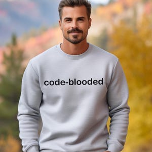Op de afbeelding: Een grijs sweatshirt met de tekst "code-blooded" in zwart op de voorkant.