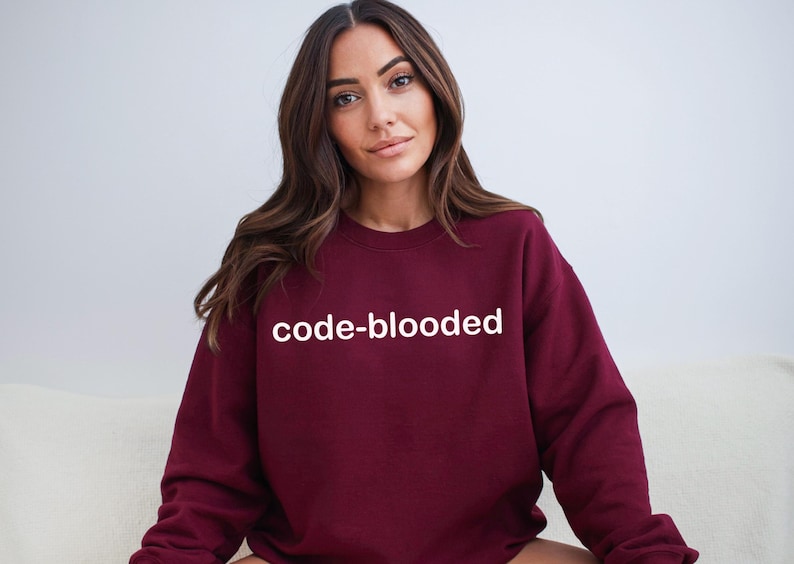 Op de afbeelding: Een bordeauxrood sweatshirt met de tekst "code-blooded" in wit gedrukt op de voorkant.