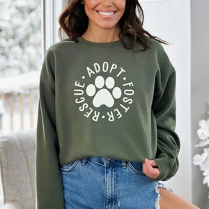 May include: A green sweatshirt with a white paw print and the text "Adopt. Foster. Rescue." in a circle around the paw print.