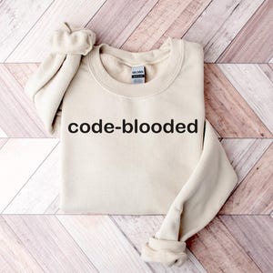 Op de afbeelding: Een beige sweatshirt met de tekst "code-blooded" in het zwart op de voorkant.