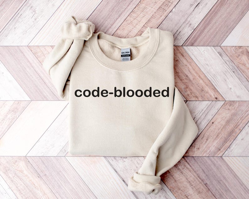 Op de afbeelding: Een beige sweatshirt met de tekst "code-blooded" in het zwart op de voorkant.