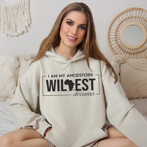 May include: A light beige hoodie with a black graphic print that says "I am my ancestors wildest dreams" with an outline of the continent of Africa.