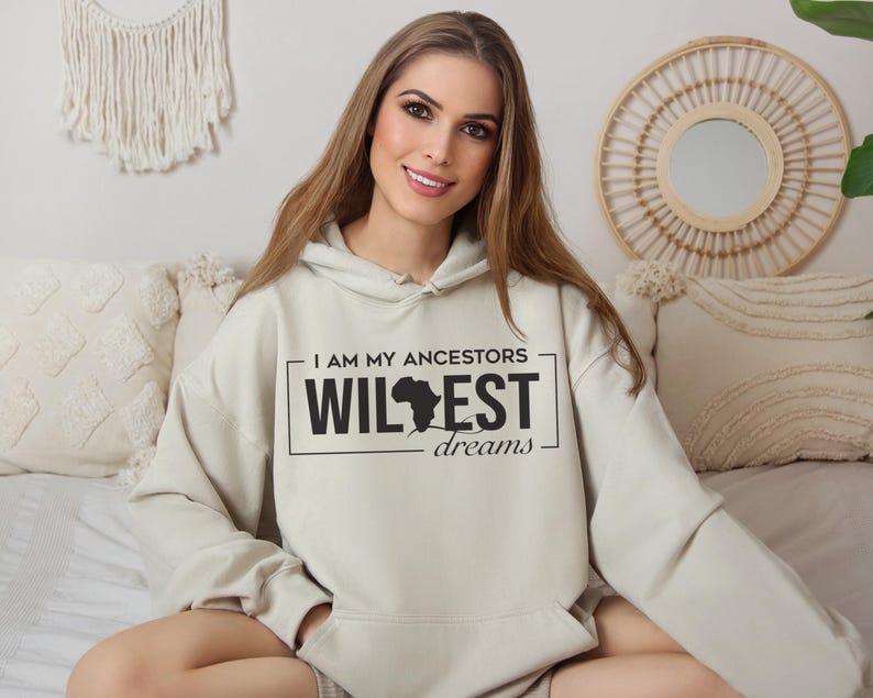 May include: A light beige hoodie with a black graphic print that says "I am my ancestors wildest dreams" with an outline of the continent of Africa.