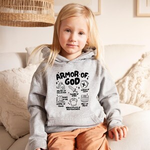 May include: A grey hoodie with a black graphic print of the Armour of God. The graphic includes a helmet, shield, sword, shoes, belt, and breastplate. The text reads "Armour of God" and lists the different pieces of armour.