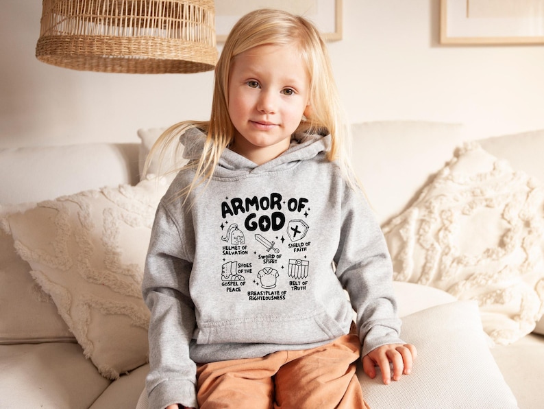 May include: A grey hoodie with a black graphic print of the Armour of God. The graphic includes a helmet, shield, sword, shoes, belt, and breastplate. The text reads "Armour of God" and lists the different pieces of armour.