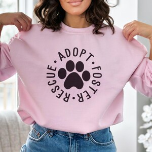 May include: Pink sweatshirt with a black paw print and the text "Adopt. Foster. Rescue." in a circle.