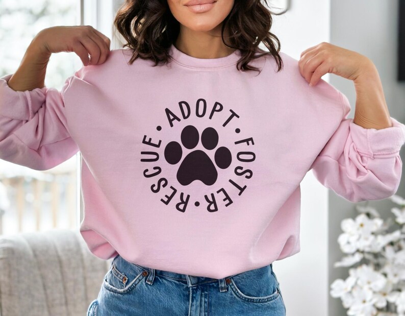 May include: Pink sweatshirt with a black paw print and the text "Adopt. Foster. Rescue." in a circle.