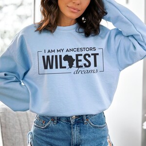 May include: A light blue sweatshirt with a black graphic print that says "I am my ancestors wildest dreams" with an outline of the continent of Africa.