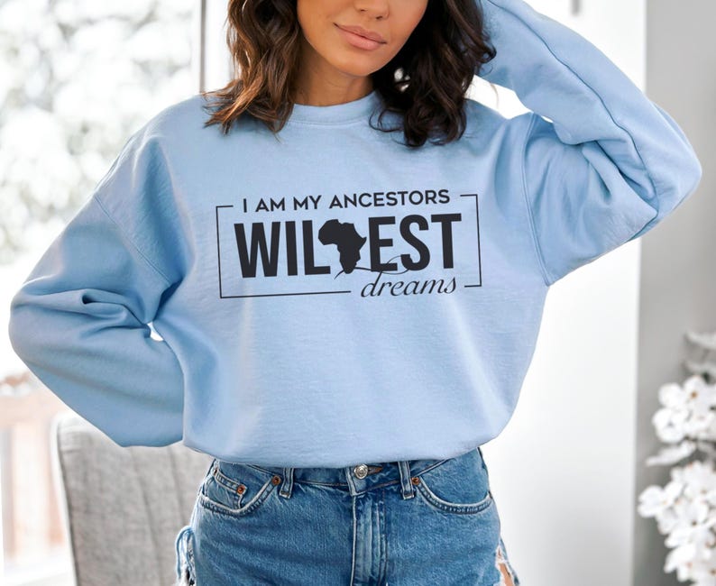 May include: A light blue sweatshirt with a black graphic print that says "I am my ancestors wildest dreams" with an outline of the continent of Africa.