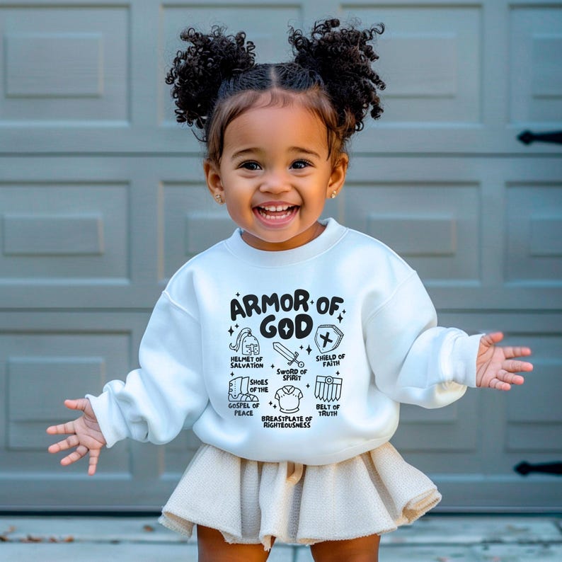 May include: A white sweatshirt featuring a black graphic of the Armour of God. The graphic includes a helmet, sword, shield, shoes, breastplate, and belt. The text "Armour of God" is written in a bold, black font.