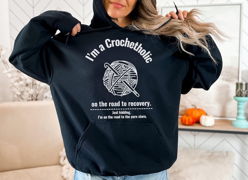 K&ouml;nnte beinhalten: Schwarzer Kapuzenpullover mit dem Text "I'm a Crochetholic" &uuml;ber einer Garnkugel und H&auml;kelhaken-Grafik. Unter der Grafik steht der Text "on the road to recovery. Just kidding. I'm on the road to the yarn store."