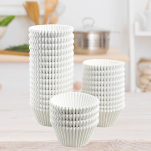 May include: A collection of white paper cupcake liners arranged in three distinct stacks of varying heights. Each liner features a pleated, fluted design with a circular opening at the top, constructed from thin, lightweight paper material.