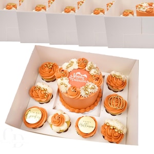 May include: An orange frosted cake and cupcakes in a white box. The cake is decorated with white frosting, gold sprinkles, and a "Happy Halloween" message. The cupcakes have orange frosting and gold sprinkles. The box is white.