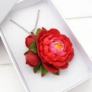 May include: A red and pink peony flower pendant necklace with green leaves. The necklace is made of polymer clay and is on a silver chain.