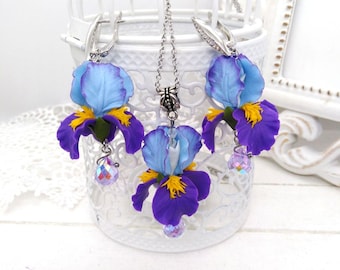 May include: A purple and blue iris flower necklace and earrings set with crystal accents. The necklace has a silver chain and a pendant with a purple and blue iris flower. The earrings are silver hoops with purple and blue iris flowers.