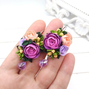 Puede incluir: Un par de pendientes florales con flores de arcilla polimérica rosa, púrpura y lavanda. Los pendientes tienen un colgante de cristal.