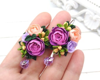 Op de afbeelding: Een paar bloemenoorbellen met roze, paarse en lavendelkleurige polymer clay bloemen. De oorbellen hebben een hangende kristallen hanger.