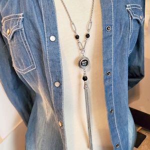 May include: A silver chain necklace with a black tassel and a round pendant featuring the words "Shift Key" in white lettering.