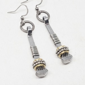 Puede incluir: Un par de pendientes de plata con un diseño de clavo de herradura. Los pendientes están acentuados con alambre dorado y pequeñas cuentas de plata.