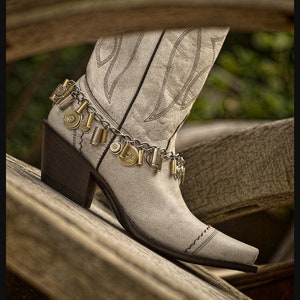 May include: White leather cowboy boot with a decorative ankle bracelet made of a chain and metal bullet casings.
