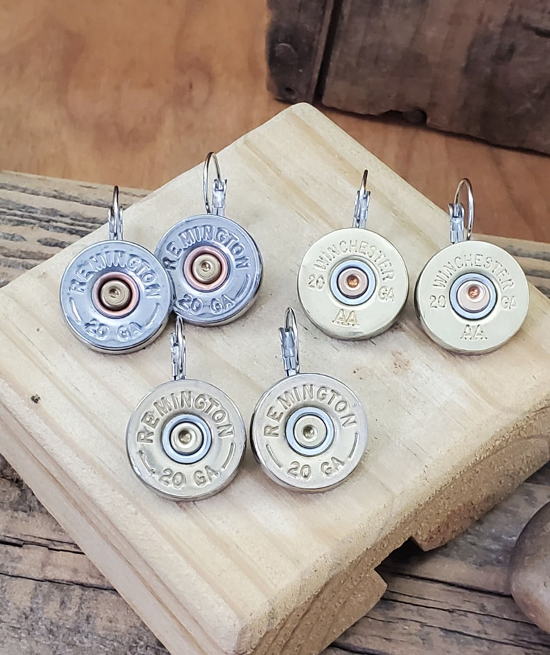 May include: Six pairs of silver and gold tone earrings featuring shotgun shell casings with the words "Remington" and "Winchester" printed on them. The casings are 20 gauge.