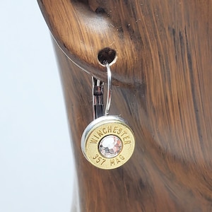 Op de afbeelding: Zilveren creolen met een gouden hanger in de vorm van een patroonhuls met een heldere strasssteen en de tekst "WINCHESTER 357 MAG".