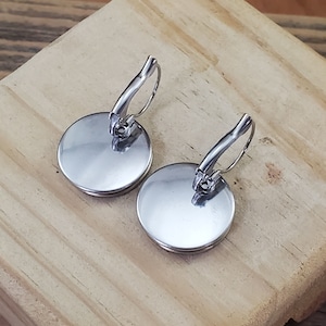 May include: A pair of silver earrings with round, smooth, silver discs. The earrings have a lever back closure.