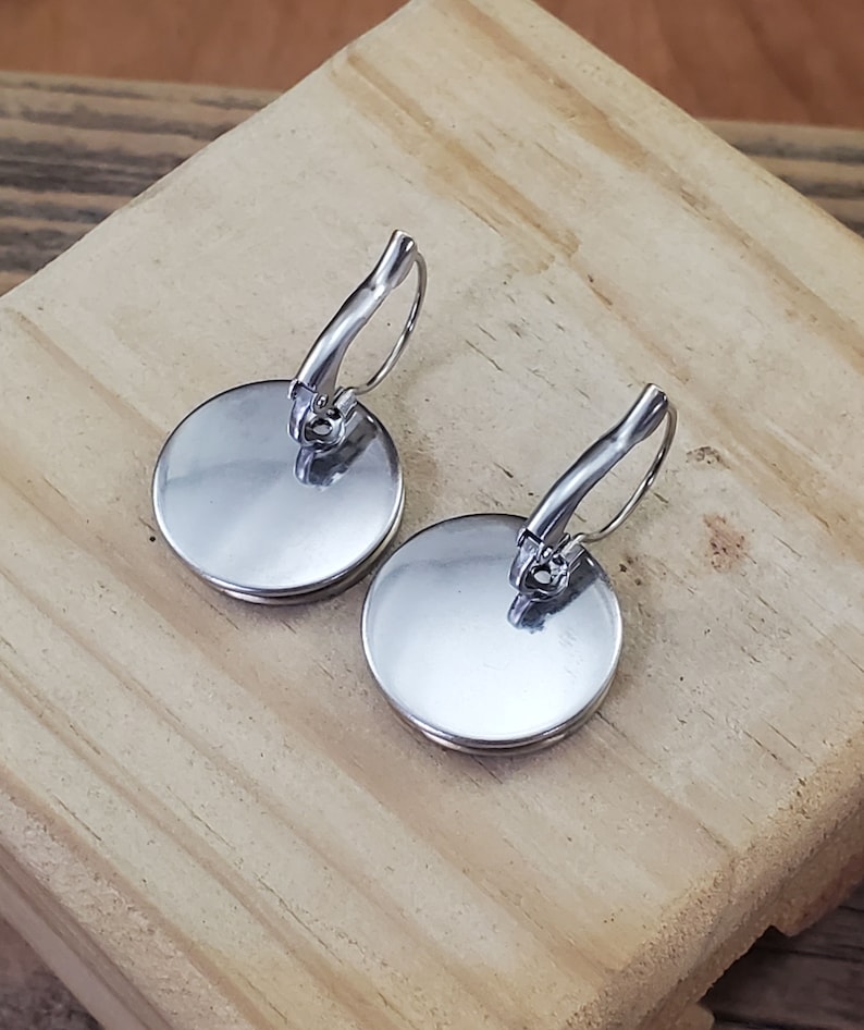 May include: A pair of silver earrings with round, smooth, silver discs. The earrings have a lever back closure.
