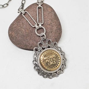May include: A silver chain necklace with a round pendant featuring a gold medallion with the text "Missouri Pacific Lines".