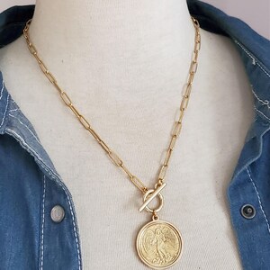 May include: A gold chain necklace with a large gold coin pendant featuring an angel design. The chain is a simple, linked style.