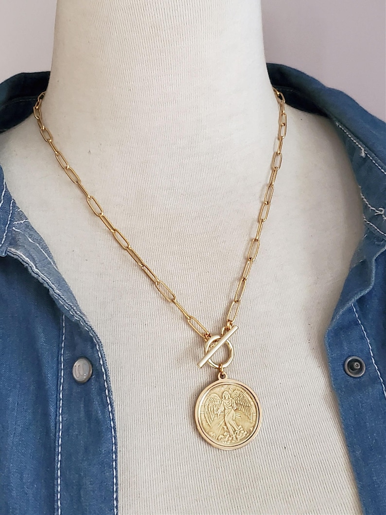 May include: A gold chain necklace with a large gold coin pendant featuring an angel design. The chain is a simple, linked style.