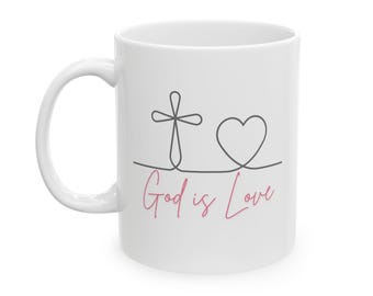 Peut inclure: Une tasse en céramique blanche avec un motif de croix et de cœur noir et le texte "God is Love" en rose.