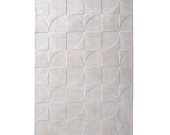 Peut inclure: Un tapis rectangulaire gris clair avec un motif géométrique. Le design présente des carrés et des demi-cercles disposés en grille. Le tapis a un aspect doux et texturé, adapté à la décoration intérieure.