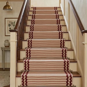 May include: A staircase with a runner rug featuring horizontal stripes in shades of beige and red. The edges of the runner have a zigzag pattern in a darker red. The stairs have wooden steps and white risers, with a dark brown handrail.
