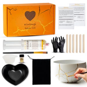 May include: A Kintsugi repair kit featuring an orange box with gold veining, a dual-chamber epoxy resin syringe, black gloves, wooden mixing sticks, a brush, a small measuring cup, gold powder, a black drawstring bag, and a heart-shaped bowl.