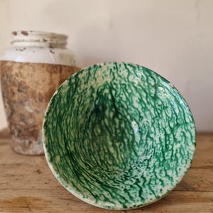 Può includere: Una ciotola in ceramica caratterizzata da un vivace motivo marmorizzato o a goccia verde e bianco sulla superficie interna. La ciotola presenta un bordo circolare e una forma profonda, con una finitura strutturata in varie tonalità di verde.