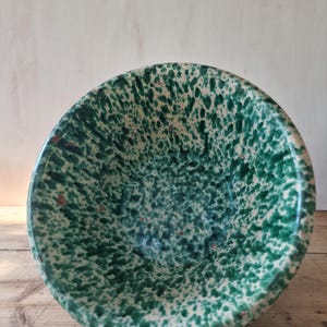 Può includere: Una ciotola in ceramica rotonda caratterizzata da un motivo maculato con schizzi di vernice verde scuro su una base color crema. La ciotola presenta un bordo circolare ampio e aperto e un interno profondo, con una texture uniforme.