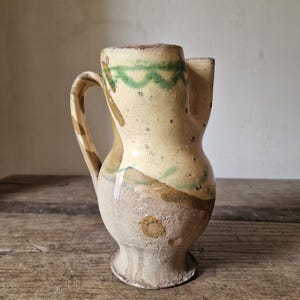 Könnte beinhalten: Eine weiße Keramik-Tasse mit schwarzem Henkel und dem Text "But First, Coffee" in fetter, schwarzer Schrift. Die Tasse steht vor einem verschwommenen Hintergrund, der eine gemütliche Umgebung andeutet.