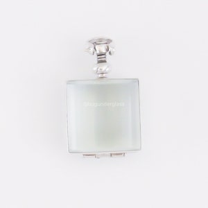 May include: A silver locket pendant with a square, frosted glass insert. The locket has a hinged lid and a decorative top.