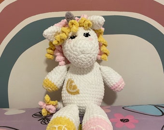 May include: A white crocheted unicorn stuffed animal with yellow and pink accents. The unicorn has a yellow horn, yellow and pink mane, and a yellow lemon design on its chest.
