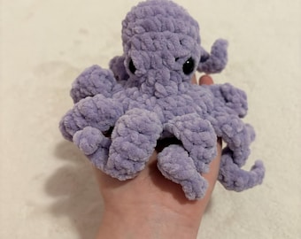 May include: A handmade, lavender-colored crochet octopus with black eyes. The plush toy has eight curled tentacles and a rounded head. The soft, textured yarn gives the octopus a cuddly appearance.